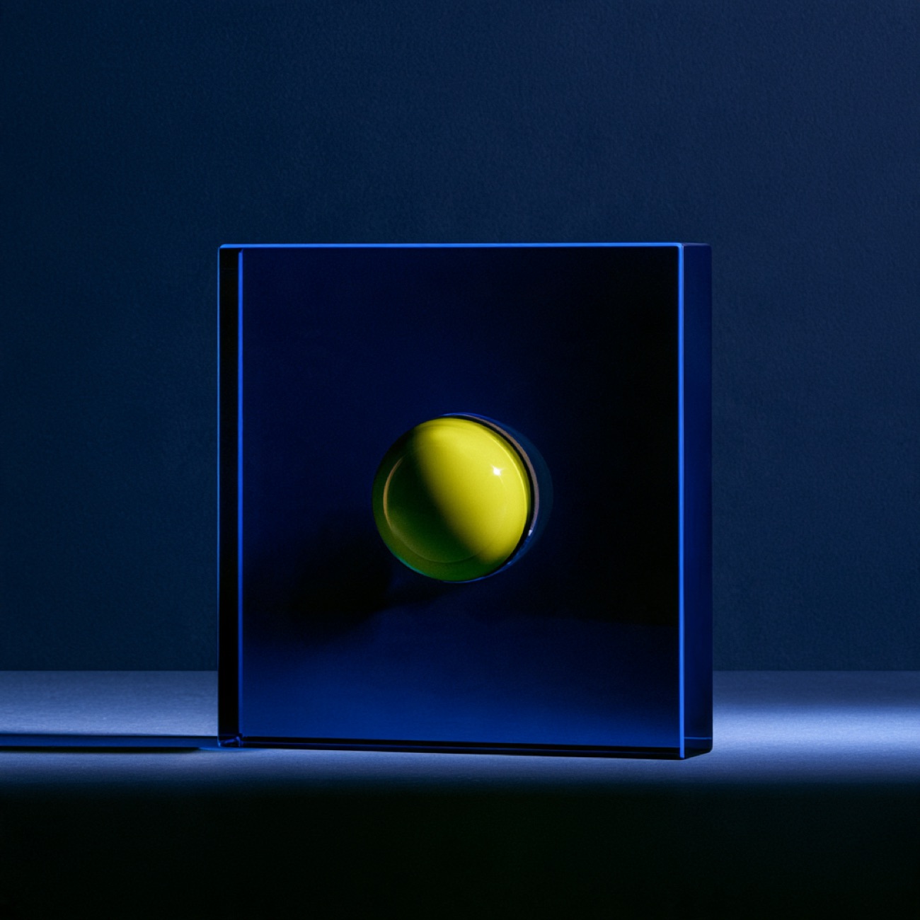 Blauer Glasblock mit eingelassenem gelben Ball vor dunklem Hintergrund